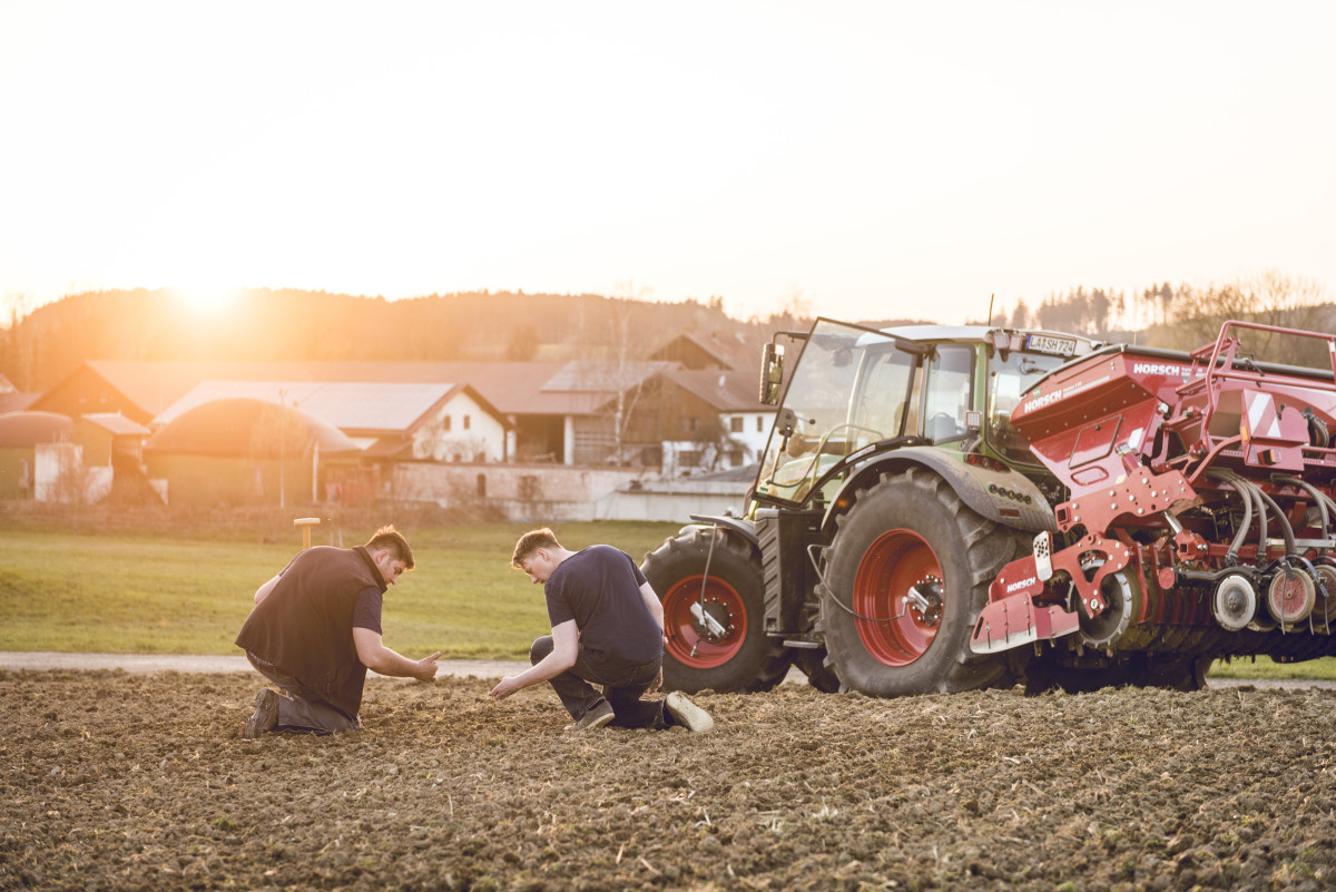 zwei Landwirte knien auf seinem Feld, daneben steht ein Traktor