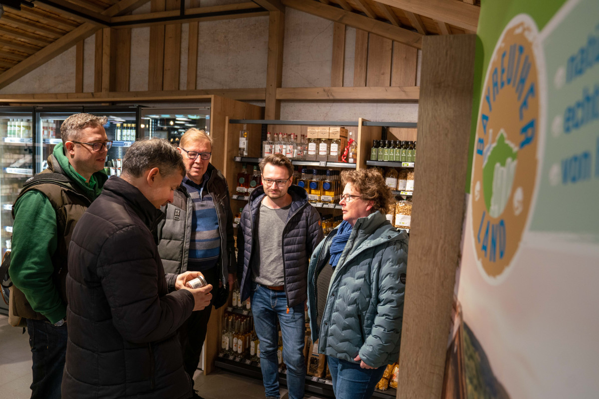 Marion Deinlein und Besucher stehen im Hofladen und betrachten die Regionalprodukte.